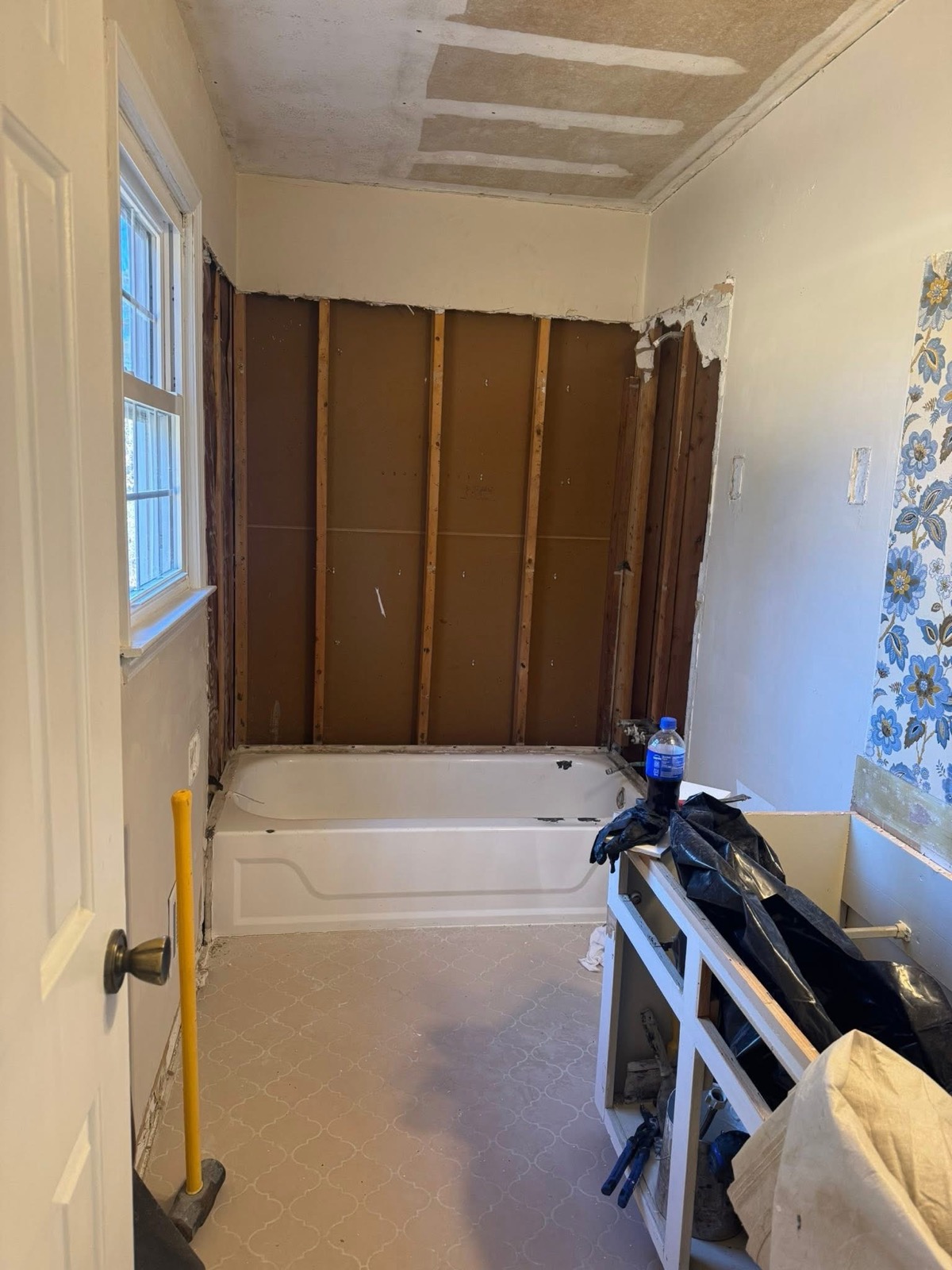 Bathroom mid-demo before remodeling, with exposed wall studs behind a bathtub and unfinished surfaces.