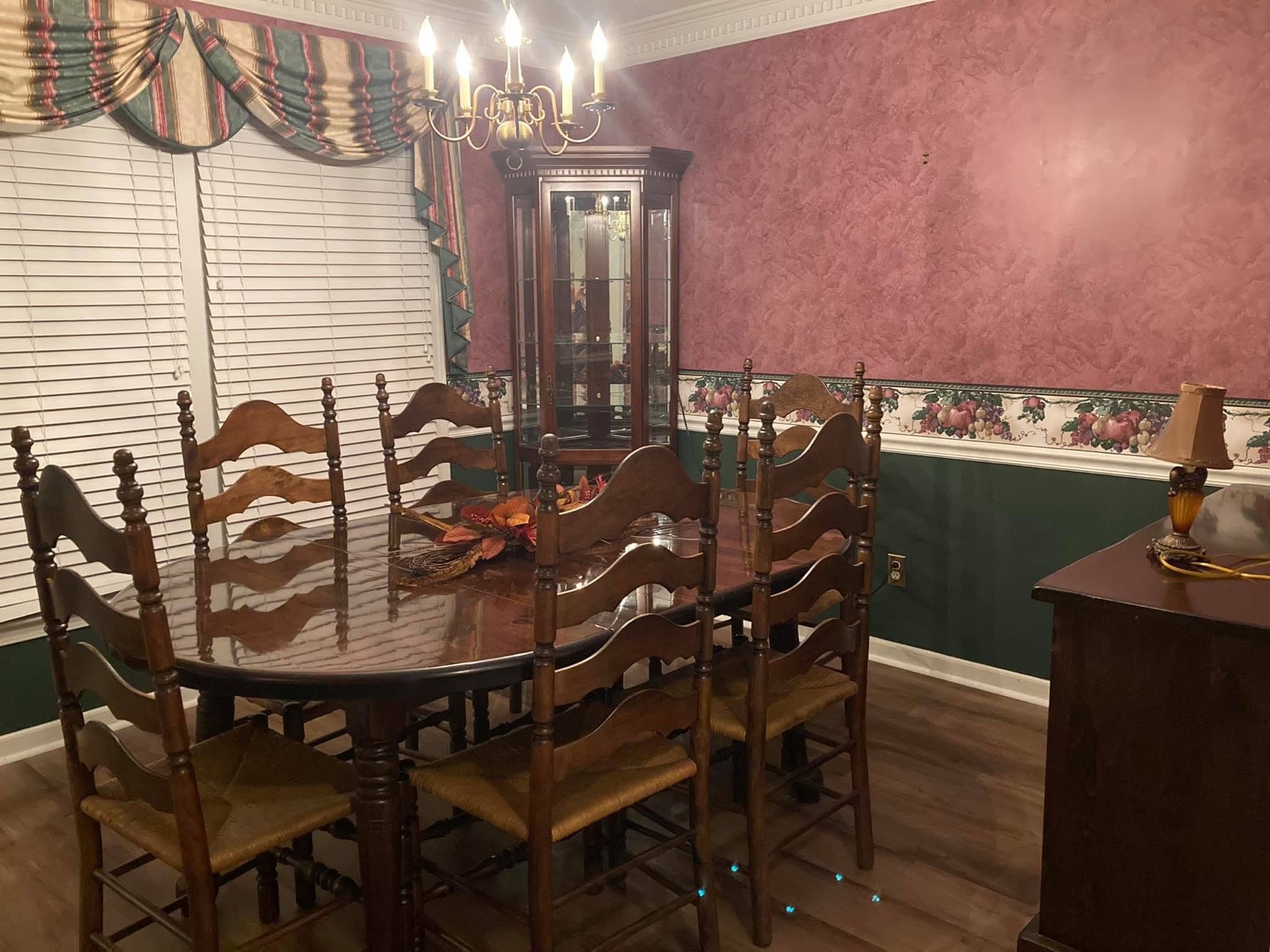 Traditional dining room before painting, with red faux-finish walls, green wainscoting, and a floral wallpaper border.