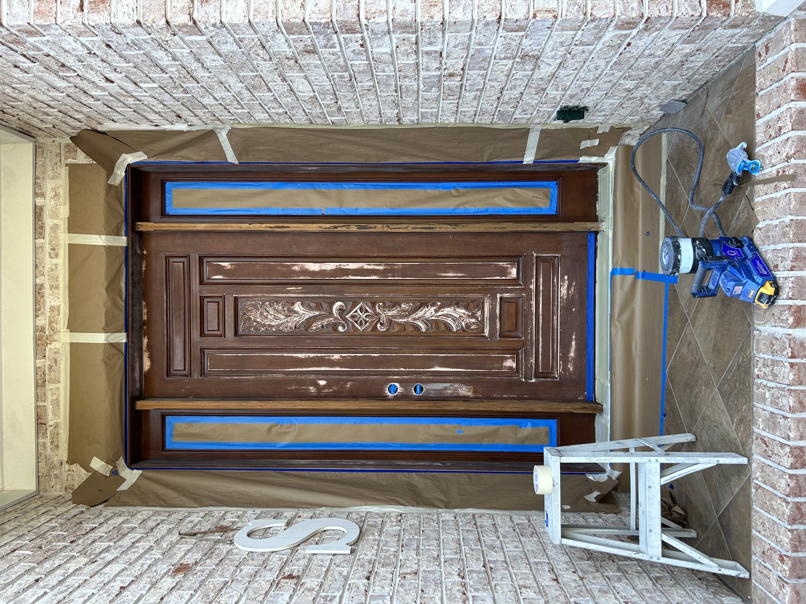 Front entry door in progress before refinishing, with a brown wood tone and masking around the frame.