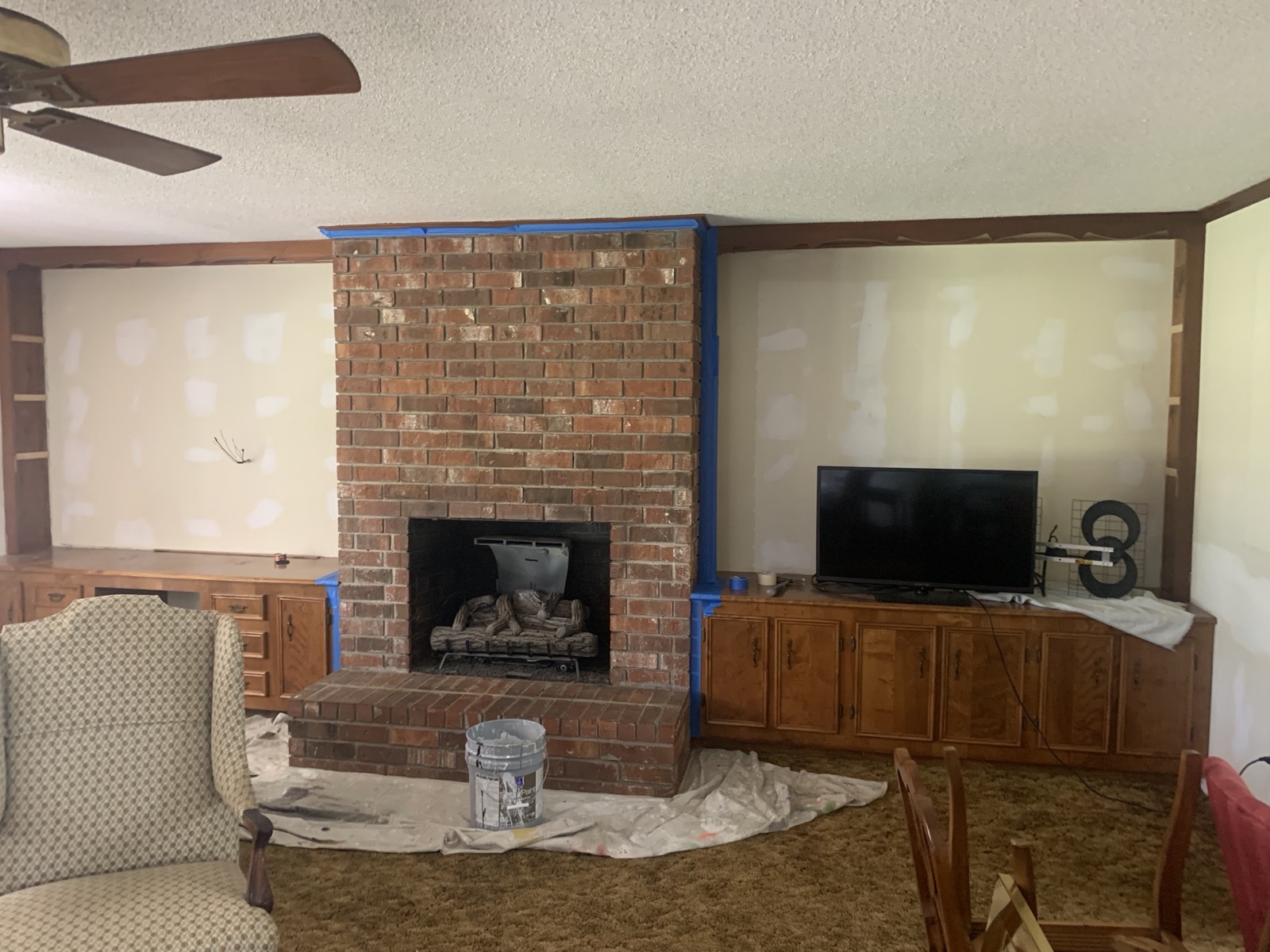 Living room brick fireplace wall before paint, with exposed brick and stained wood trim.