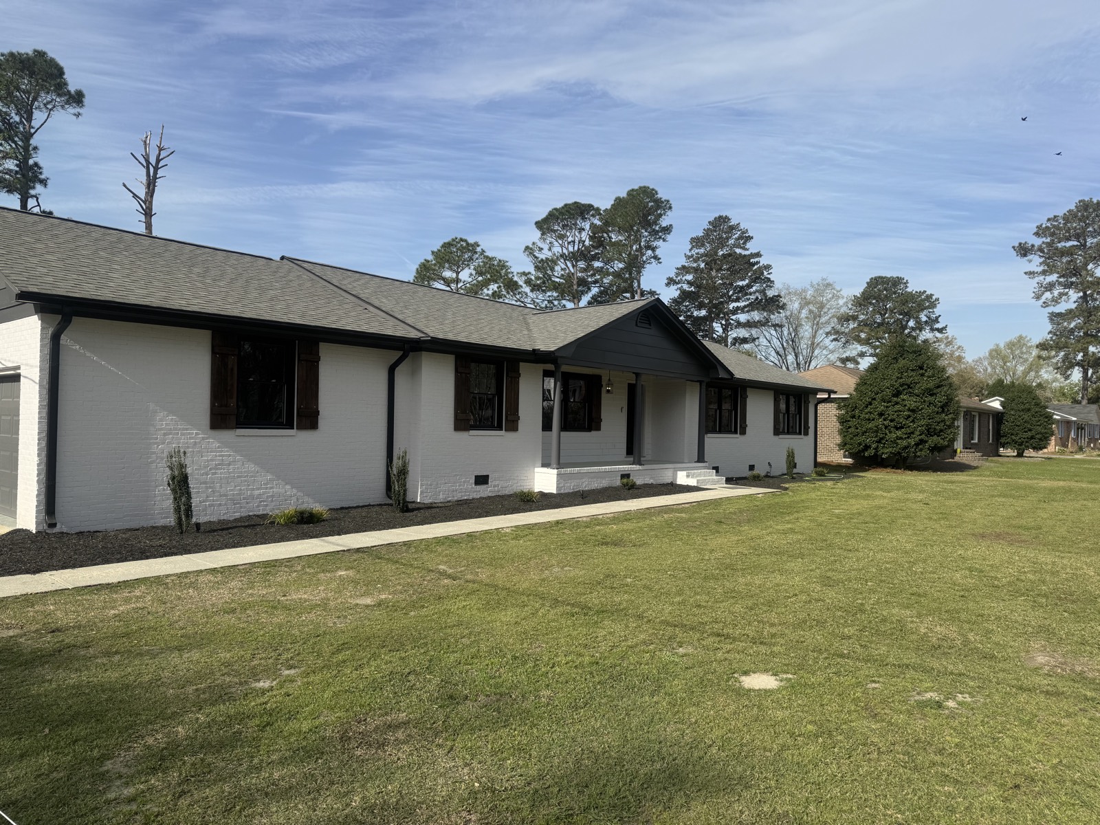 The same ranch home after repainting with white brick, dark trim, and refreshed landscaping.