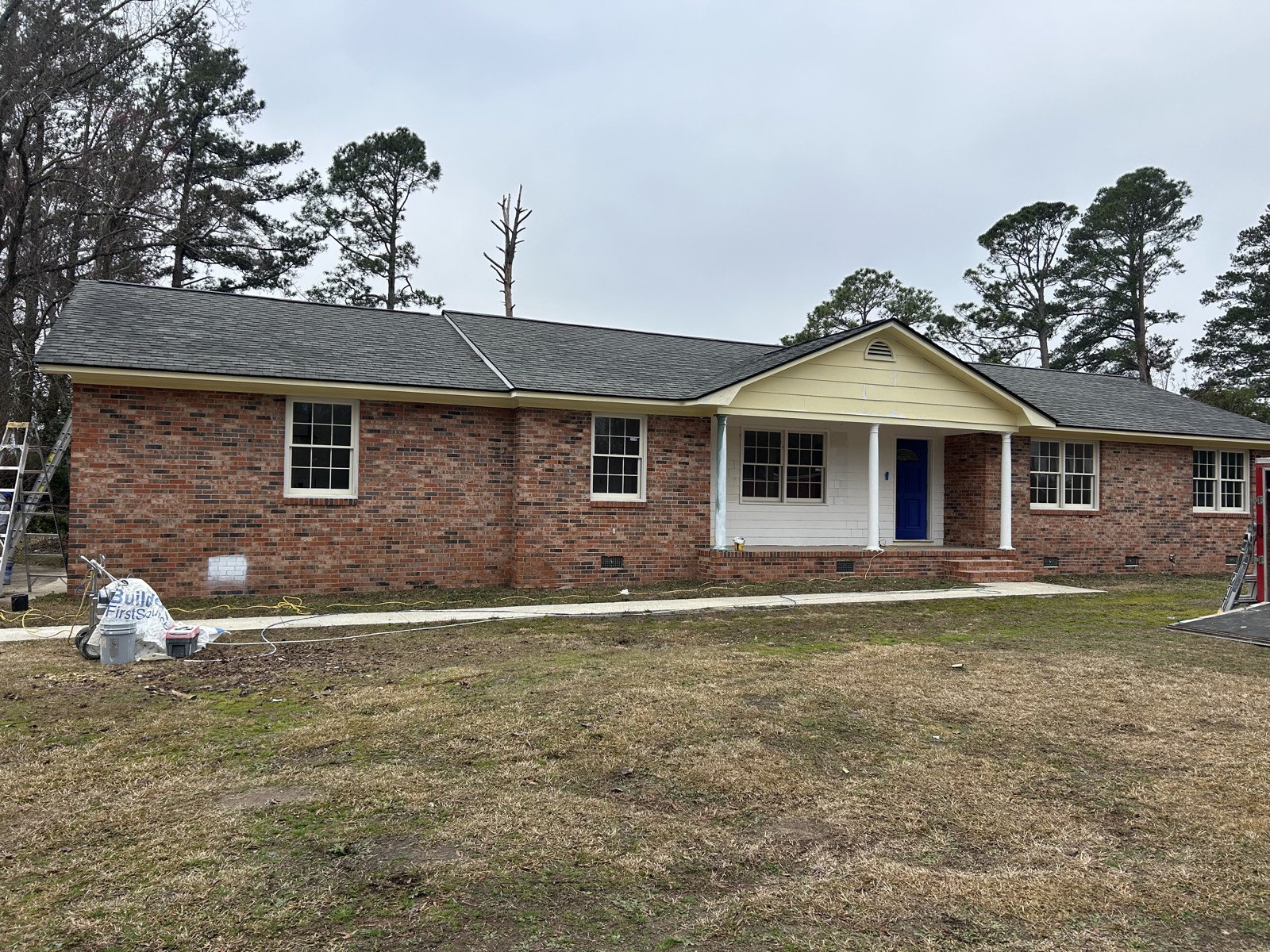 Single-story brick ranch home before the repaint with tan siding accents and a blue front door.
