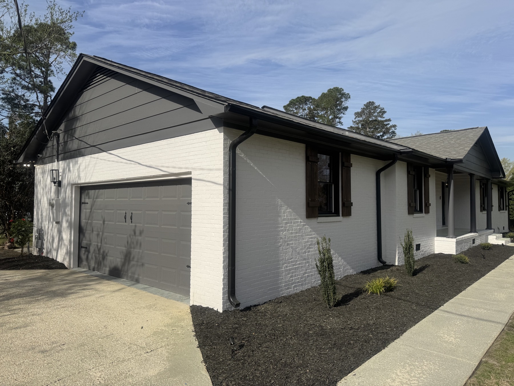 Freshly painted brick ranch home with white exterior, dark trim, and refreshed landscaping.