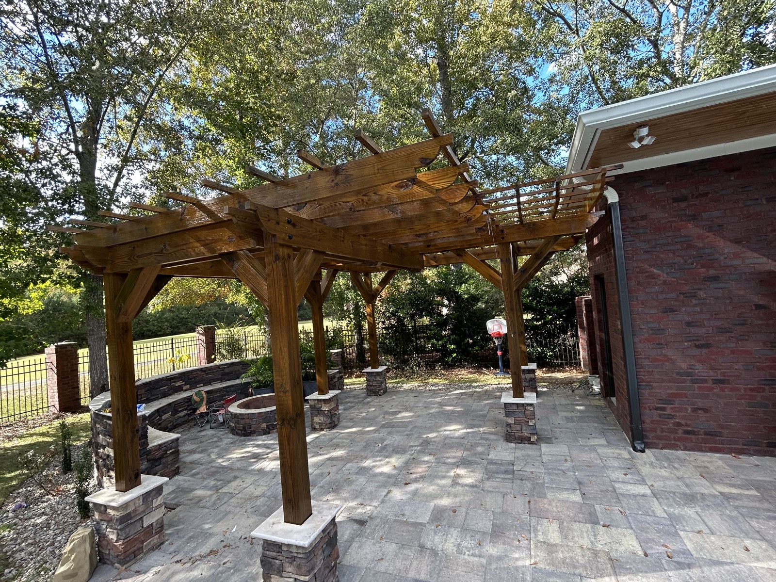 Custom stained wood pergola over a backyard patio with stone column bases.
