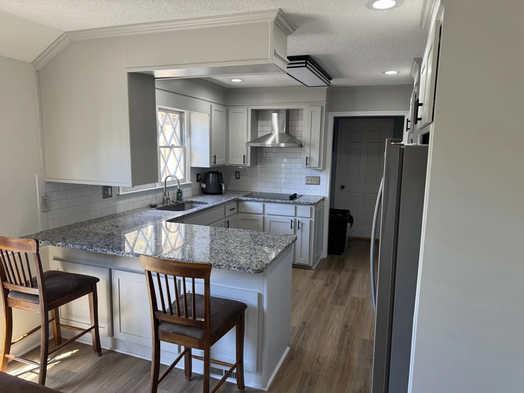 Finished kitchen with painted cabinets, shaker-style doors, white tile backsplash, and a stainless hood vent.