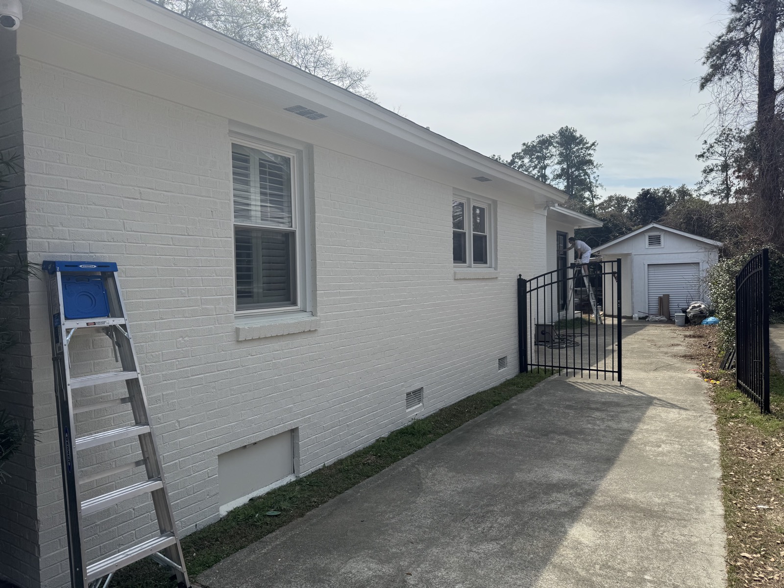House exterior in progress with ladder and prep work along the painted brick wall.